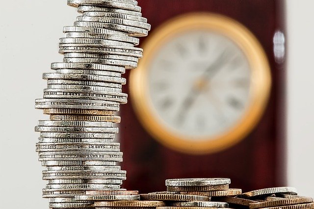 Imagen de una montaña de monedas junto a un reloj grande de pared